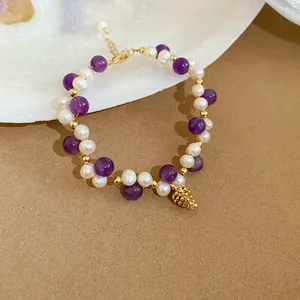 Close-up of elegant bracelet featuring purple amethyst beads, freshwater pearls, and a pinecone charm