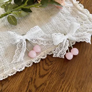 Elegante weiße Spitzen-Haarspangen mit rosa Harzkirsch-Anhängern auf einem Tisch.