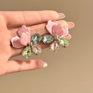 Close-up of oversized pink enamel and colorful crystal flower earrings held in hand