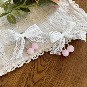 Nahaufnahme von weißen Spitzenbögen-Haarklammern mit rosa Kirschanhängern aus Harz