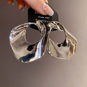 Primo piano di orecchini geometrici cavi in argento oversize con finitura lucida.