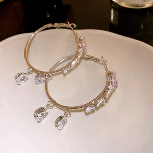 Close-up detail of silver hoop earrings with zircon butterfly and teardrop pendants