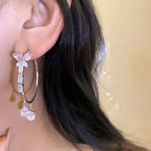 Detailed close-up of a silver hoop earring featuring a zircon butterfly and teardrop charms.
