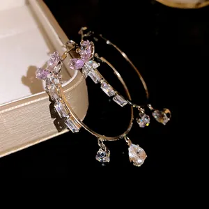 Close-up detail of silver needle hoop earrings with pink butterfly and zircon drops.