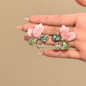 Close-up of exaggerated pink flower stud earrings with colorful teardrop crystals