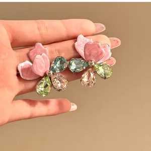 Close-up of pink flower earrings featuring colorful teardrop crystals on a warm background