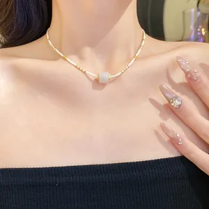 Nahaufnahme eines weißen Perlen-Chokers mit einem Steinanhänger am Hals des Models