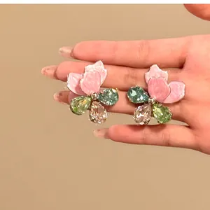 Detailed macro view of colorful rhinestone flower stud earrings held for scale demonstration