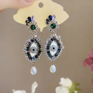 Detailed macro view of dark style rhinestone Evil Eye earrings with white teardrop pearl