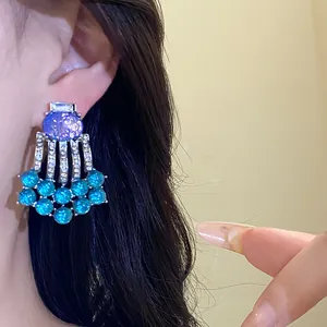Close-up of vintage resin tassel earrings with blue stones and silver needles on ear.