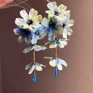 Gros plan d'élégantes boucles d'oreilles fleurs en tissu bleu clair avec gouttes en cristal.