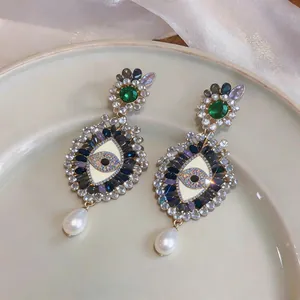 Macro view of crystal-encrusted evil eye earrings with drop pearls