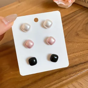 Detailed view of three pairs of square pearl stud earrings in white, pink, and black.