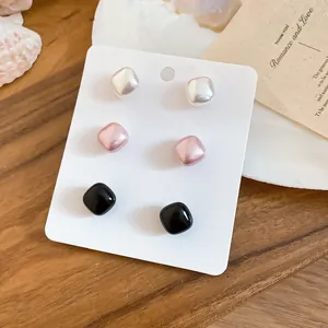 Close-up of three pairs of vintage square pearl stud earrings in white, pink, and black.
