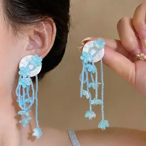 Detailed view showing light blue floral beaded tassel earrings on model and hand