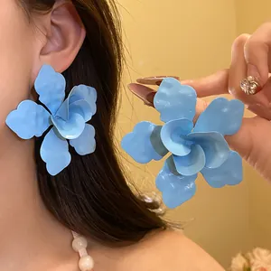 Primer plano de pendientes de flor azul mate puestos en la oreja y en la mano