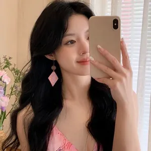 Detail of pink wooden diamond-shaped earrings with bohemian patterns on an Asian model.