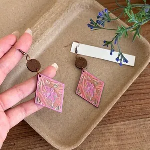 Detail shot of bohemian wooden rhombus earrings with pink embossed floral pattern.