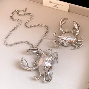 Detailed view of silver metallic crab pendant necklace and matching brooch accessory