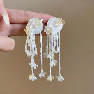 Detailed macro view of white beaded tassel earrings with cream resin flower charms