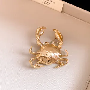 Detailed close-up of a golden 3D crab brooch featuring unique hammered metal texture
