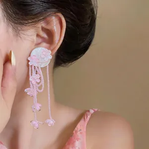 Close-up detail view of elegant pink flower tassel earrings with beaded design on a model.
