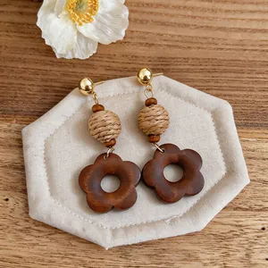 Close-up of vintage wooden flower earrings with woven bead details on a fabric pad.