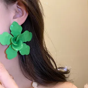 Primer plano de un pendiente de flor verde con gota de aceite en la oreja de modelo.