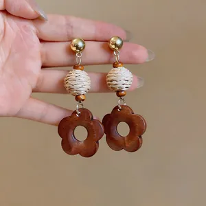 Detailed view of retro ethnic earrings featuring a woven straw ball and wooden flower pendant