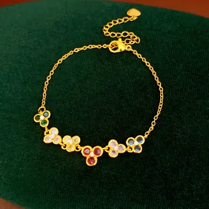 Detail view of golden chain bracelet with six colorful zircon flower charms on green velvet