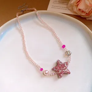 Gros plan d'un collier en perles roses avec un pendentif étoile scintillant et perle.