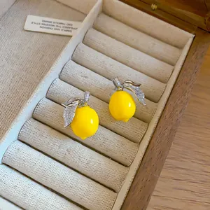 Dettaglio orecchini a lobo limone con foglie in zircone in un portagioie in legno.