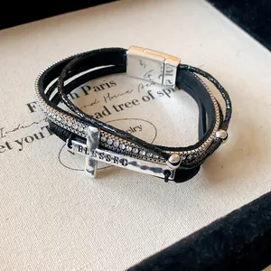 Dettaglio del bracciale multicapa in pelle bohémien con croce di strass e incisione Blessed