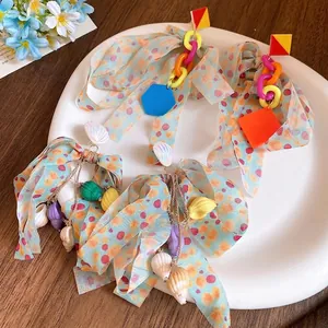 Resort style colorful bow tassel earrings with shell and conch charms on white plate