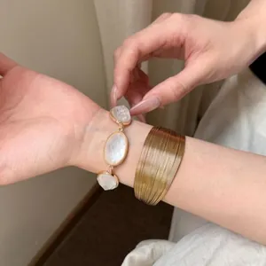 Dettaglio ravvicinato di un polsino dorato in stile bohémien e bracciale con pietre ovali