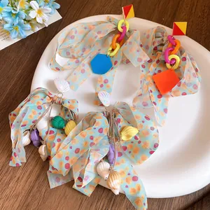 Close-up of colorful bow earrings with sea shell charms and geometric plastic links