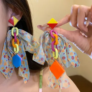 Detail of colorful geometric earrings with large fabric bow tassels and silver needles