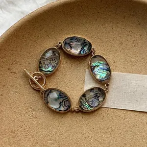 Dettaglio di un bracciale boho dorato con inserti ovali in conchiglia di abalone.