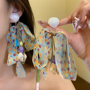 Close-up of colorful bow earrings featuring iridescent shell charms and polka dot ribbons.