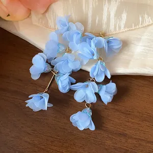 Close-up of light blue chiffon flower tassel earrings with elegant textured fabric background