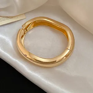 Elegante bracciale rigido minimalista in metallo lucido dorato con forma organica