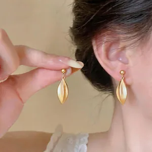 Dettaglio ravvicinato di eleganti orecchini a forma di foglia d'oro opaco dal design sobrio
