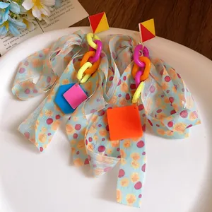 Close-up of colorful ribbon bow earrings with vibrant geometric acrylic charms and chains