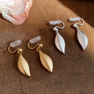 Dettaglio ravvicinato di orecchini a clip a foglia oro opaco e argento su legno