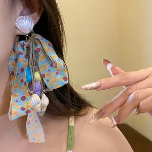 Detailed close-up of colorful bow tassel earrings with shell charms worn on a model