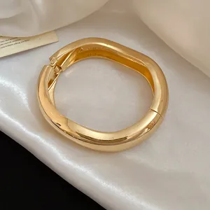 Primo piano di un bracciale rigido dorato lucido a forma di goccia su seta bianca.