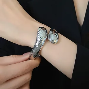 Dettaglio di un bracciale rigido aperto a goccia d'argento con texture martellata e lucida