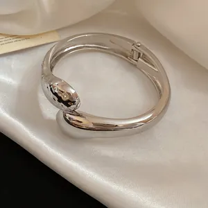 Dettaglio macro del bracciale rigido incrociato a goccia in metallo argento minimalista
