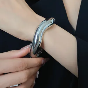 Primo piano di un bracciale a polsino in metallo argento lucido dal design fluido