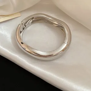Vista dettagliata di un bracciale rigido in metallo argentato lucido su seta bianca